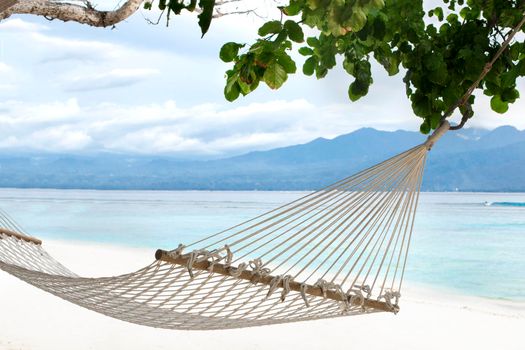 Hammock hanging between trees on a sandy beach on a background of azure Bali Sea. Coast of the Gili Trawangan island, Indonesia.