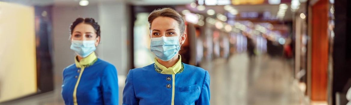 Women flight attendants wearing protective face masks and air hostess uniform while walking down airport terminal during pandemic