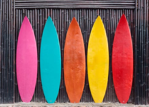 Colored surfboards leaning up against a wooden fence on beach