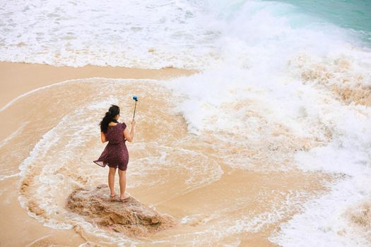 Female traveler taking selfie at the beach. Back view