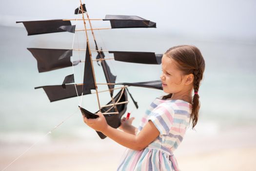 Cute little girl playing on the beach flying ship kite. Child enjoying summer family vacation at the sea.