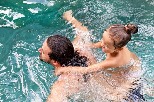 Happy family, active father with little child, adorable toddler girl, having fun together in outdoors swimming pool in water park during sunny summer sea vacation in tropical resort.