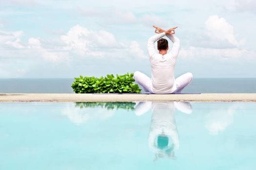 Caucasian man in white clothes meditating yoga on the sea shore pier or platform