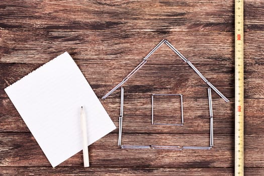 Home improvement concept - Wooden model house on a work table with tools and empty spiral notebook