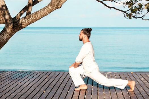 Caucasian man in white clothes meditating yoga on wooden pier