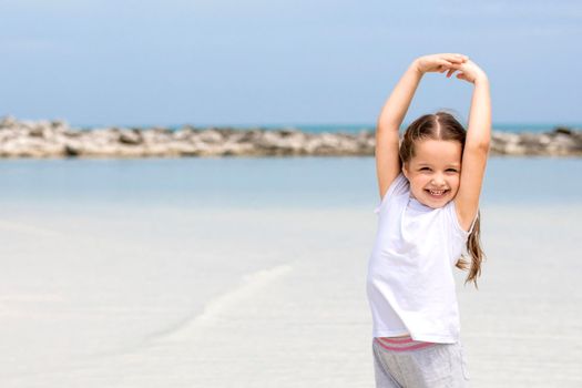 Happy child on the beach. Paradise holiday concept, girl in preschool age standing on sandy beach with blue shallow water and clean sky on background