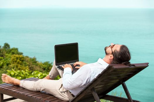 Businessman wearing a suit on deck chair typing laptop on the beach