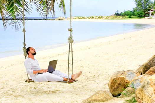 Man working with a laptop, on a hammock in the beach. Concept of digital nomad, remote worker, independent location entrepreneur. Show win