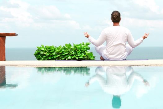 Caucasian man in white clothes meditating yoga on the sea shore pier