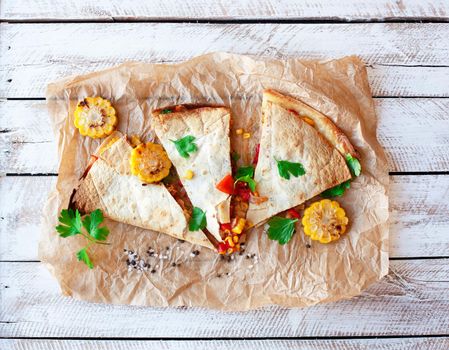 Mexican Quesadilla wrap with vegetables, corn, sweet pepper and sauces on the parchment and table. horizontal view.