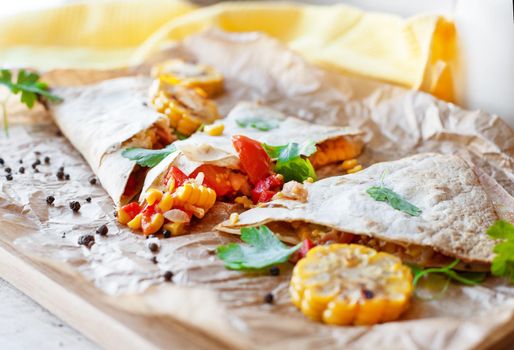 Mexican Quesadilla wrap with vegetables, corn, sweet pepper and sauces on the parchment and table. horizontal view.