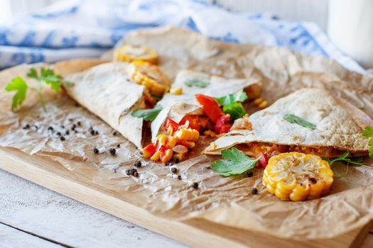 Mexican Quesadilla wrap with vegetables, corn, sweet pepper and sauces on the parchment and table. horizontal view.