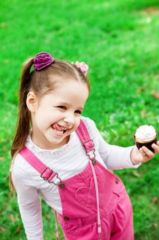 Happy little girl eating cake and having fun at the park. Child outdoor.