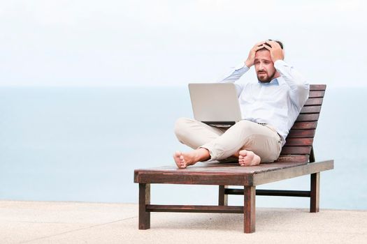 Businessman freelance on beach with laptop showing desperation, bad news.