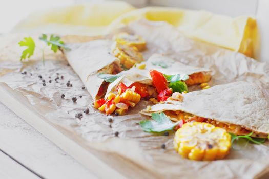 Mexican Quesadilla wrap with vegetables, corn, sweet pepper and sauces on the parchment and table. horizontal view.