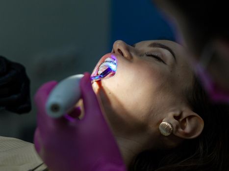 Installing a retainer after wearing braces. The process of removing braces.Beautiful woman in dental chair during procedure of installing braces to upper and lower teeth. Dentist and assistant working
