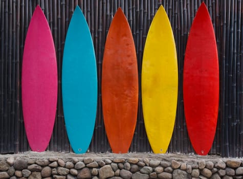 Colored surfboards leaning up against a wooden fence on beach