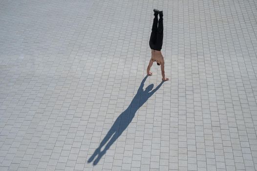 Shirtless man walks on his hands outdoors. View from above