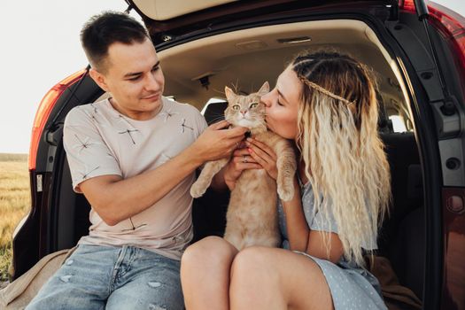 Young Woman and Man Sitting in Trunk of Car with Pet, Happy Couple with Their Red Cat Enjoying Road Trip
