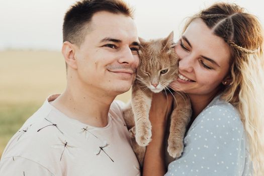 Close Up Portrait of a Happy Caucasian Couple with Red Cat, Young Woman and Man Hugging with Pet Outdoors at Sunny Summer Day