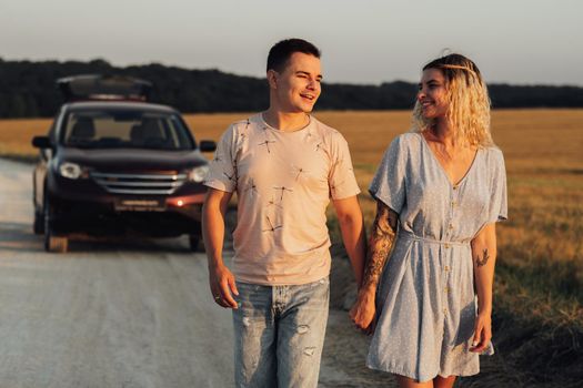 Caucasian Man and Woman Holding by Hands on Background of Their SUV Car, Young Couple Enjoying Road Trip at Sunset