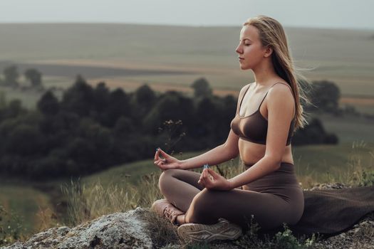 Sporty Girl Sitting in Lotus Pose and Doing Meditation Exercises on Top of Hill, Young Woman Practice Yoga Outdoors with Panoramic Landscape at Sunset