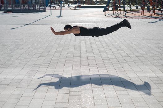 A man in black sportswear jumps while doing push-ups outdoors