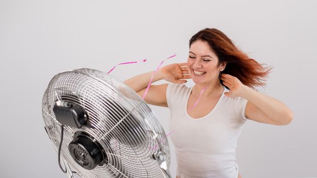 Joyful caucasian woman enjoying the wind blowing from an electric fan on a white background