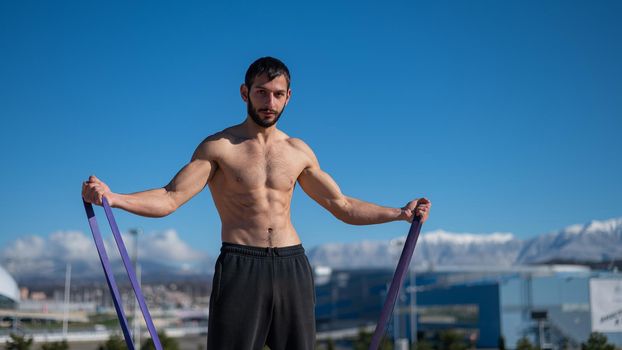 Shirtless man doing exercise with rubber bands outdoors