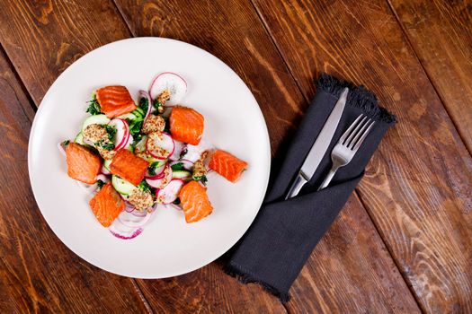 Red fish salmon with radish and spinach, served on white plate on wooden table. rustick style. View from above, top studio shot