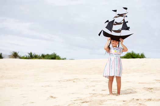 Cute little girl playing on the beach flying ship kite. Child enjoying summer family vacation at the sea.