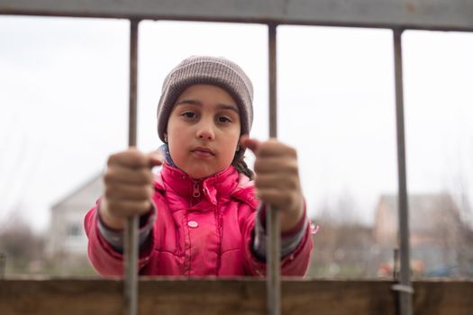 Photo of a little girl holding bars. Sad little girl behind iron bars. Little girl behind the bars. Violence concept