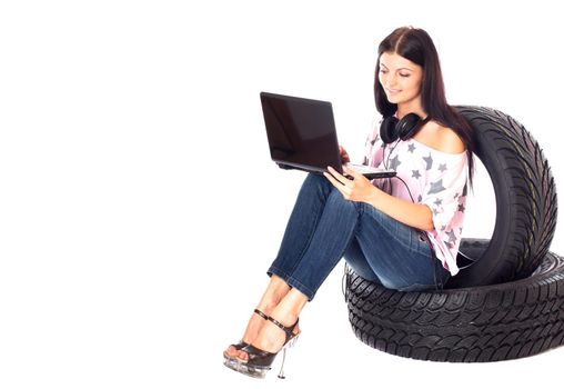 Young sexy woman with laptop and headset sitting on the car wheels, isolated on white