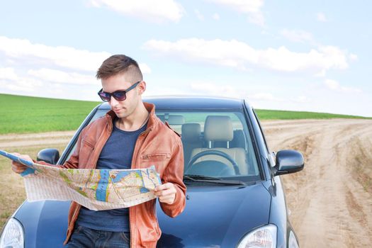 Young man reading road map near his car. lost track