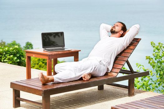 Businessman wearing white on deck chair typing laptop on the beach