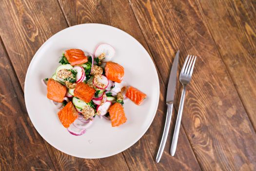 Red fish salmon with radish and spinach, served on white plate on wooden table. rustick style. View from above, top studio shot