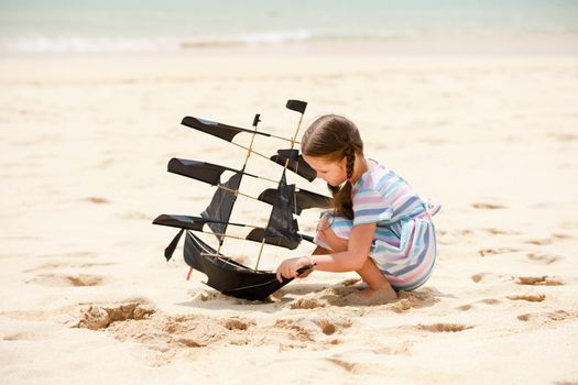 Cute little girl playing on the beach flying ship kite. Child enjoying summer family vacation at the sea.