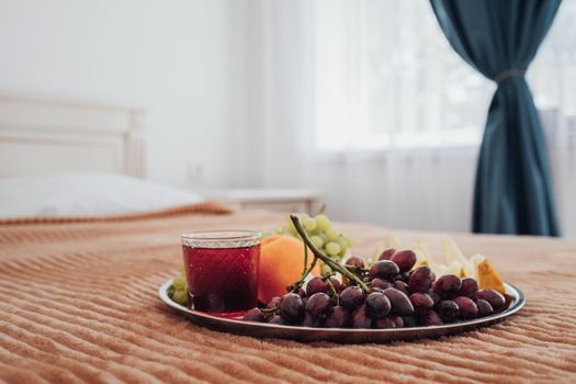 Tray of Fruit and Glass of Juice Laying on Bed in Hotel Room