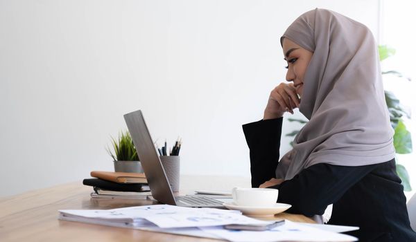 Young asian muslim business woman in smart casual wear discussing business and smiling while sitting in the creative coworking..