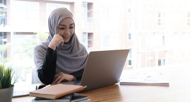 Happy beautiful muslim business woman brown hijab working about financial with business report and calculator in home office..