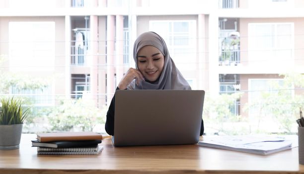 Young asian muslim business woman in smart casual wear discussing business and smiling while sitting in the creative coworking..