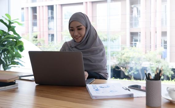 Young asian muslim business woman in smart casual wear discussing business and smiling while sitting in the creative coworking..