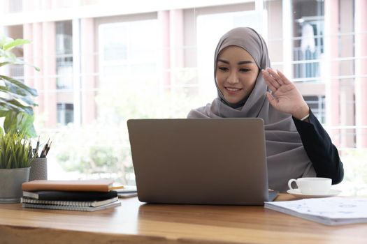 Businesswoman in hijab having a video chat on laptop while sitting at coffee shop. Female sitting at cafe and making video call using earphones and laptop computer..