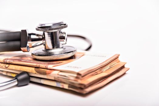 Health care costs conceptual image: stethoscope and pile of money on a medical chart, symbol of health care costs or health insurance, isolated on white background