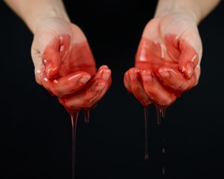 Women's hands in a viscous red liquid similar to blood