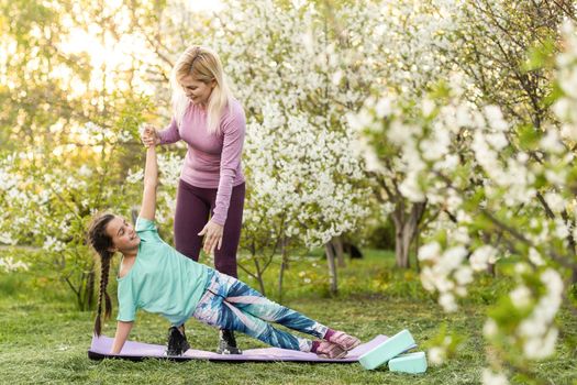 a young mother and daughter perform yoga exercises in the park on a gym mat. healthy lifestyle