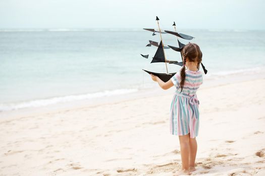 Cute little girl playing on the beach flying ship kite. Child enjoying summer family vacation at the sea.