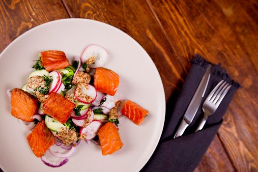 Red fish salmon with radish and spinach, served on white plate on wooden table. rustick style. View from above, top studio shot