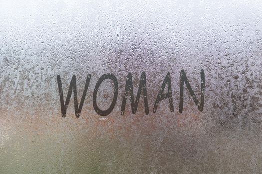Word - woman. Abstract background with drops of water. Inscription on foggy window. Handwritten text on wet glass.