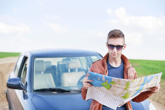 Young man reading road map near his car. lost track